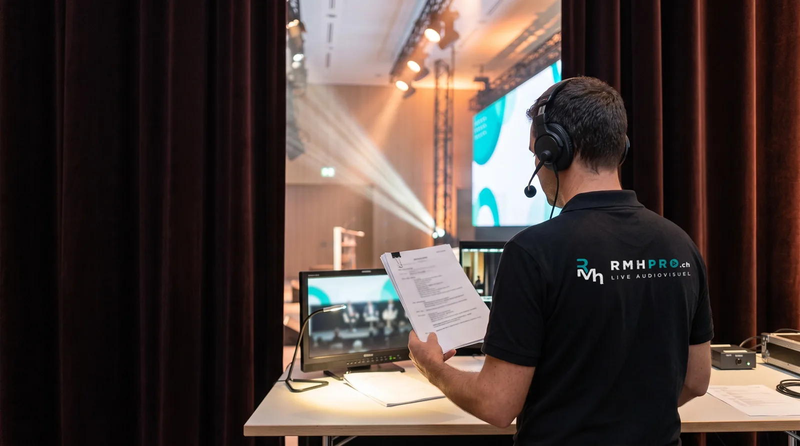 Régisseur général en polo RMHpro, casque et conducteur en main, en coulisses